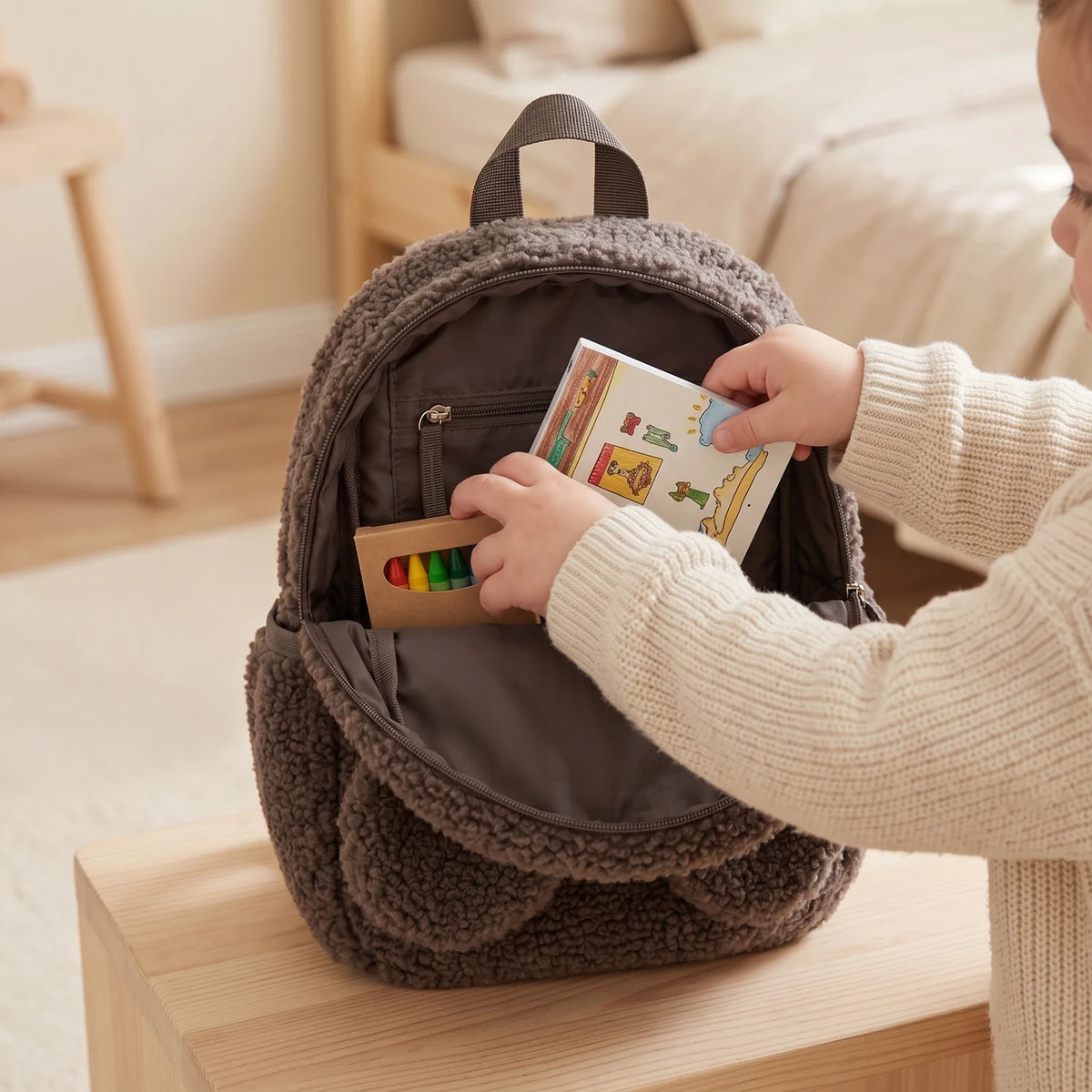 Kind packt ein Buch in den geöffneten Teddy Rucksack in Taupe
