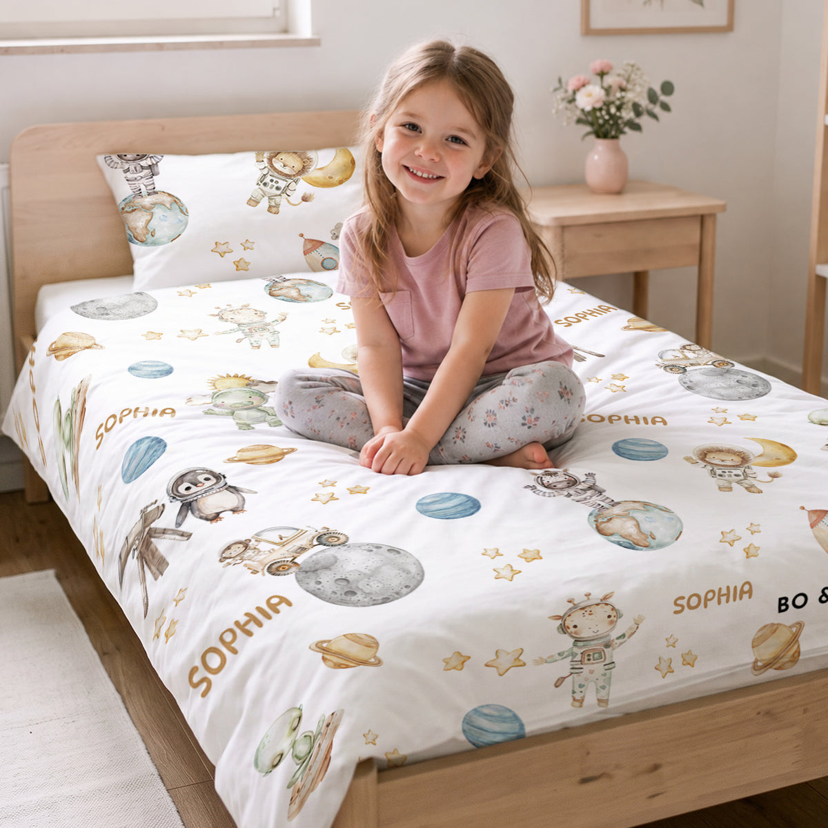 Mädchen sitzt auf dem Bett mit der Weltall-Safari-Bettwäsche