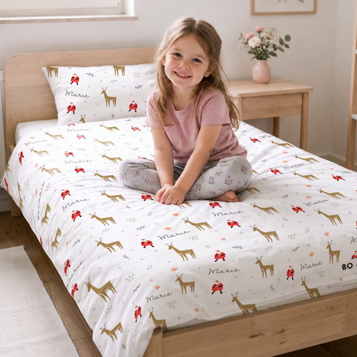 Mädchen sitzt auf dem Bett mit der Weihnachts-Bettwäsche