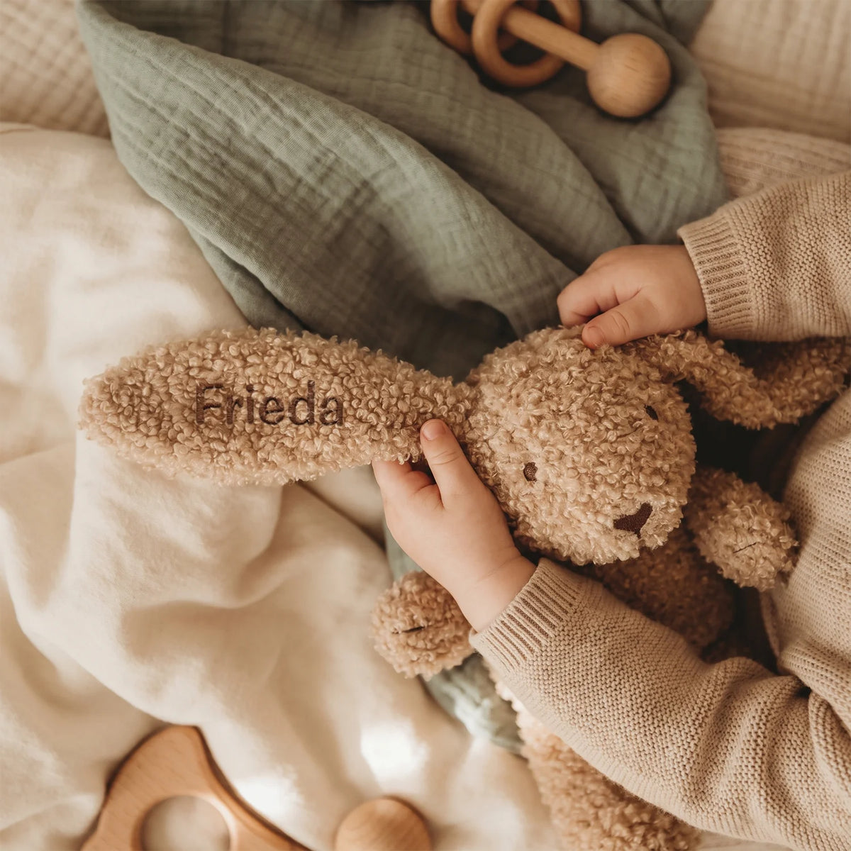 Baby greift nach dem Kuschelhasen mit dem Namen „Frieda“ auf dem Ohr