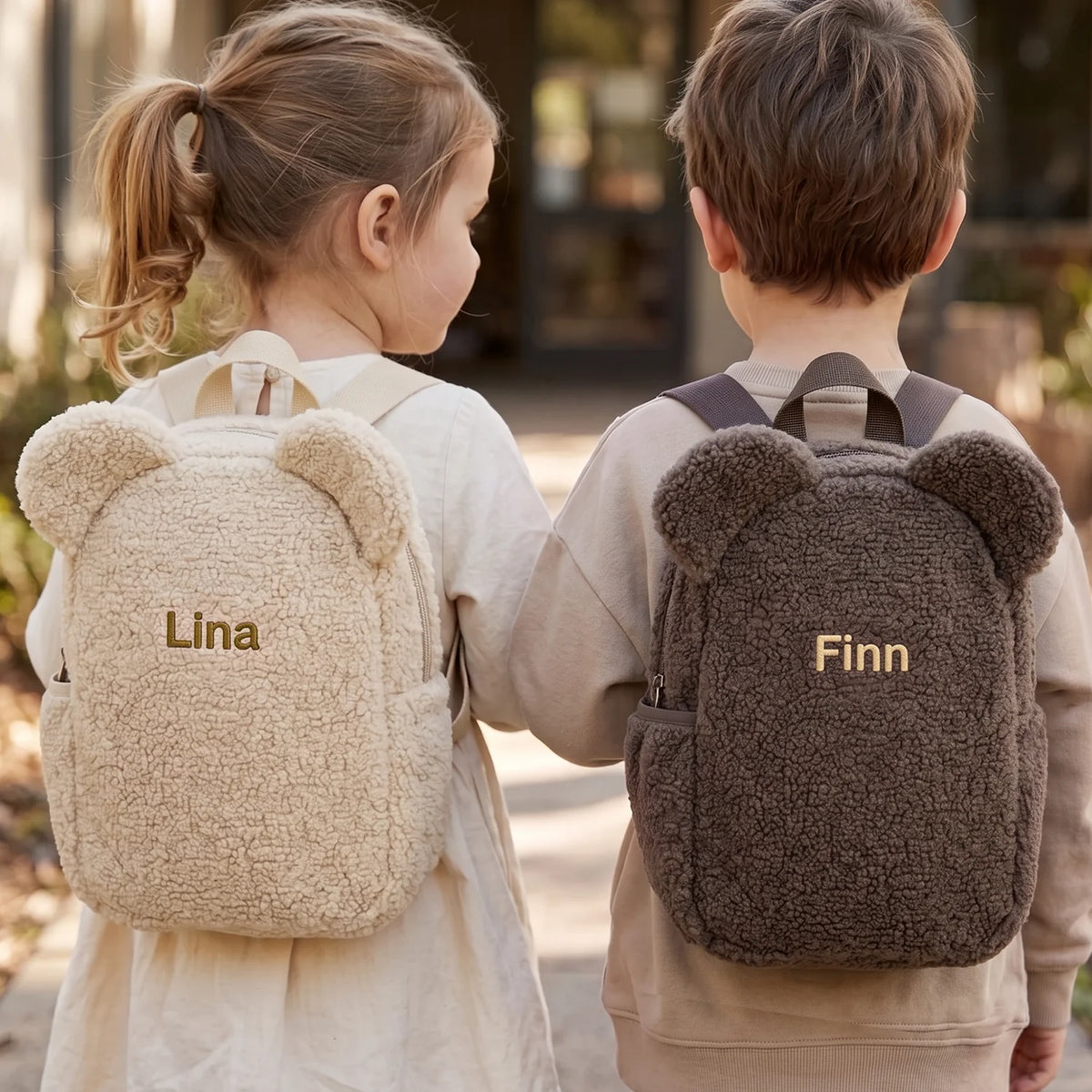 Zwei Kinder mit Teddy Rucksäcken in Beige und Taupe mit den Namen „Lina“ und „Finn“