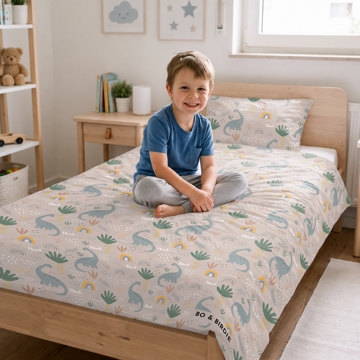 Junge sitzt auf dem Bett mit der Dinosaurier-Bettwäsche