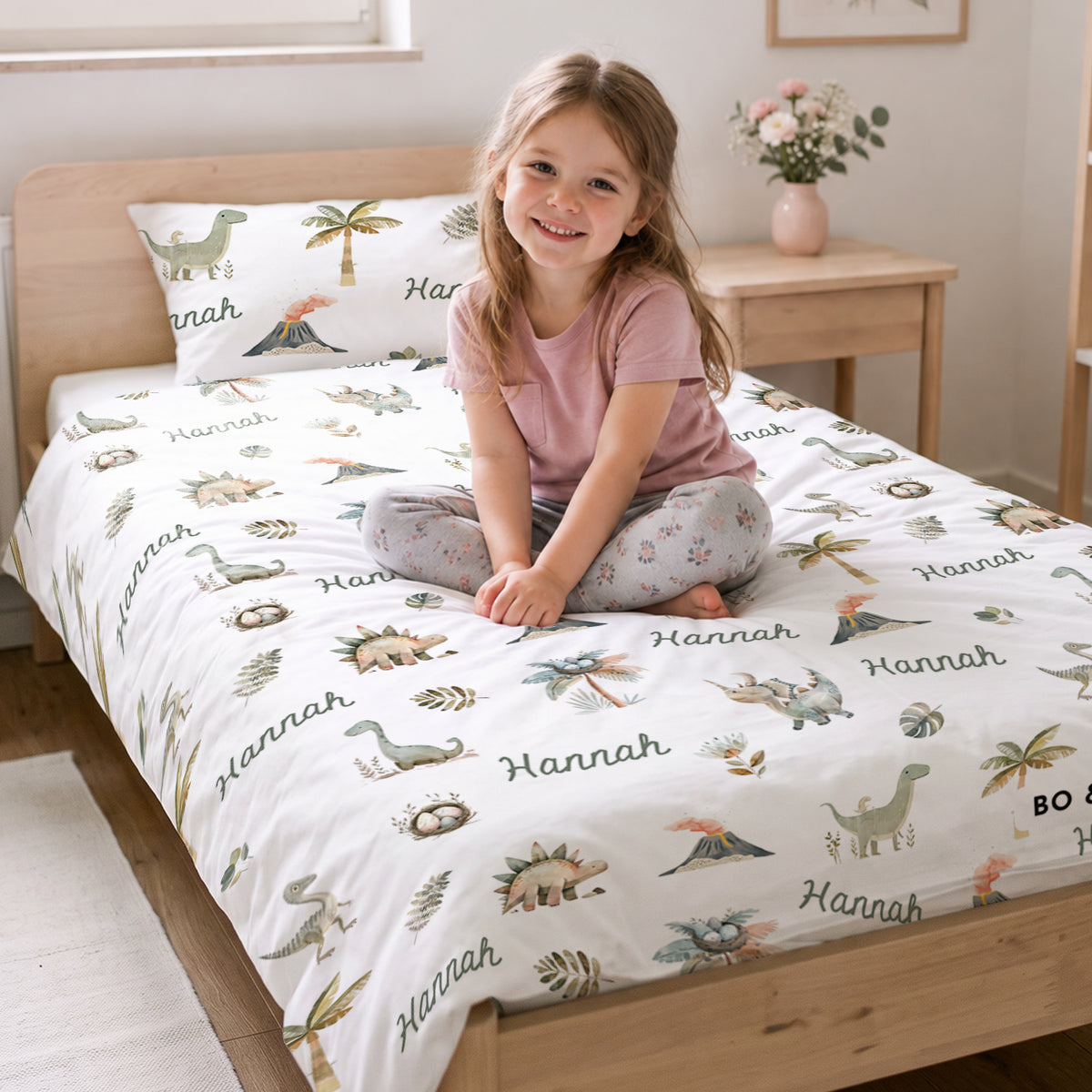 Mädchen sitzt auf dem Bett mit der Dino-Bettwäsche