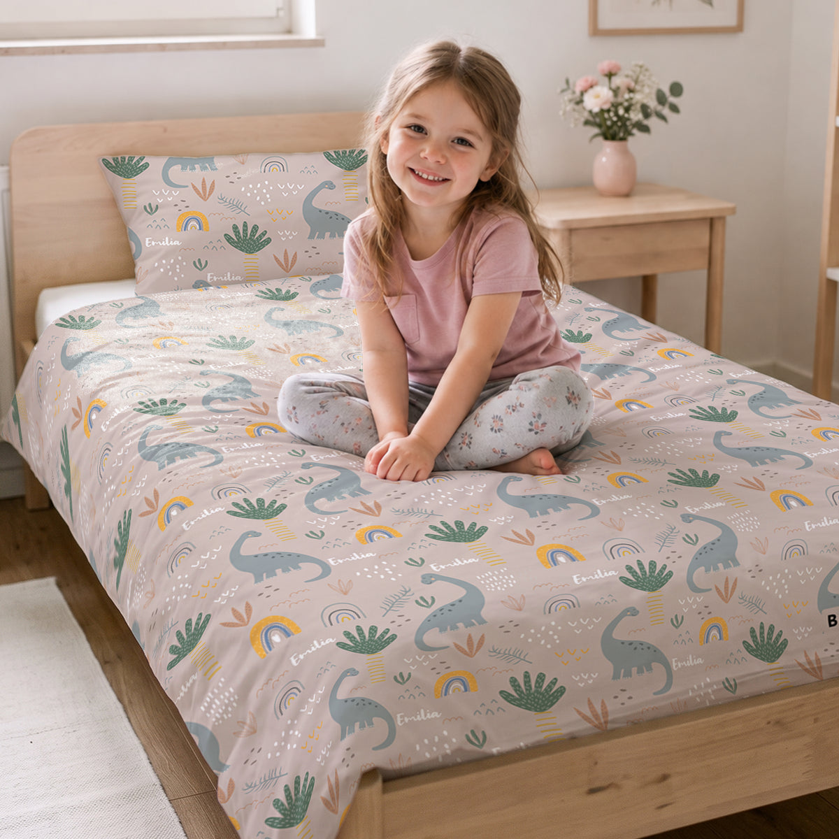 Mädchen sitzt auf dem Bett mit der Dinosaurier-Bettwäsche